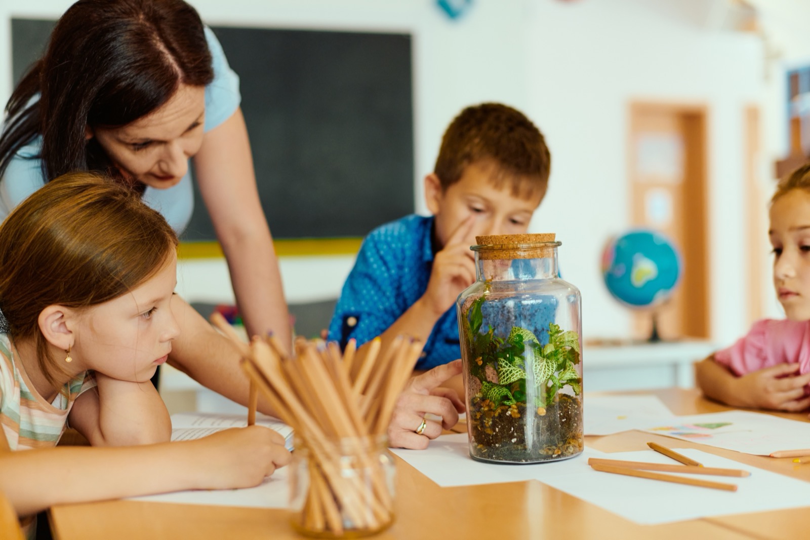 Teacher showing class a terrarium while elementary students observe and learn in classroom activity.
