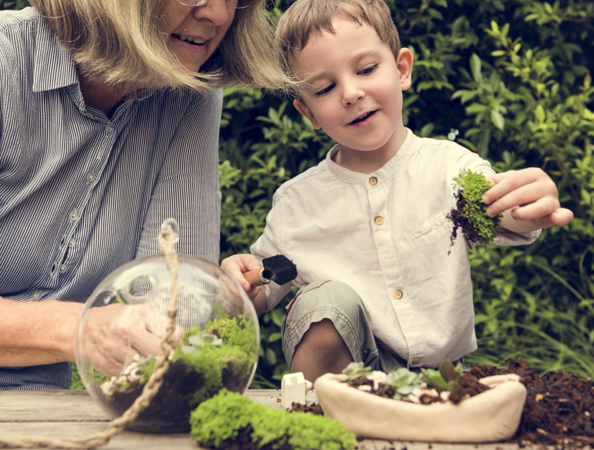 A child and woman smile as they lift a clump of moss from the dirt.