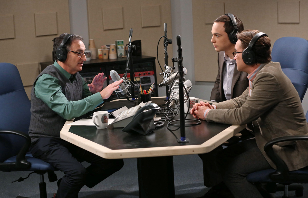 three people sitting around desk with microphones in a radio studio