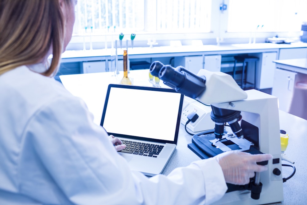 woman scientist sitting at desk with microscope and laptop