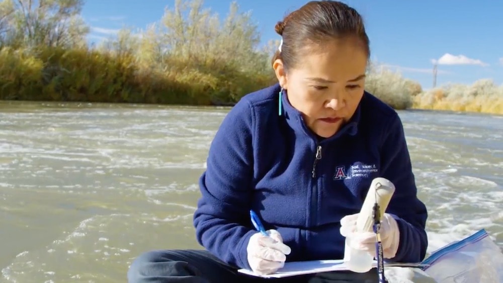 karletta chief sitting along a river bank in navajo nation recording data