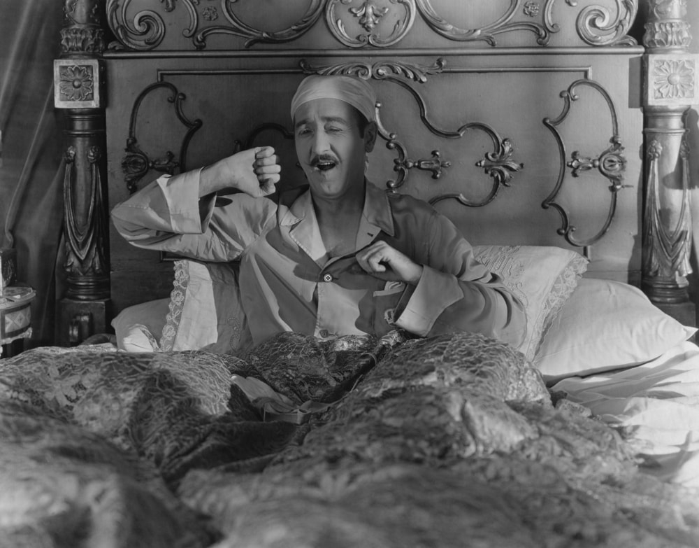 black and white man in bed with cap yawning