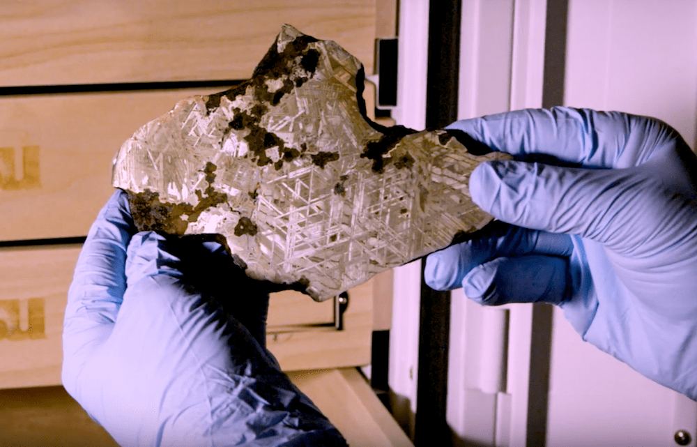 gloved hands holding shiny iron meteorite