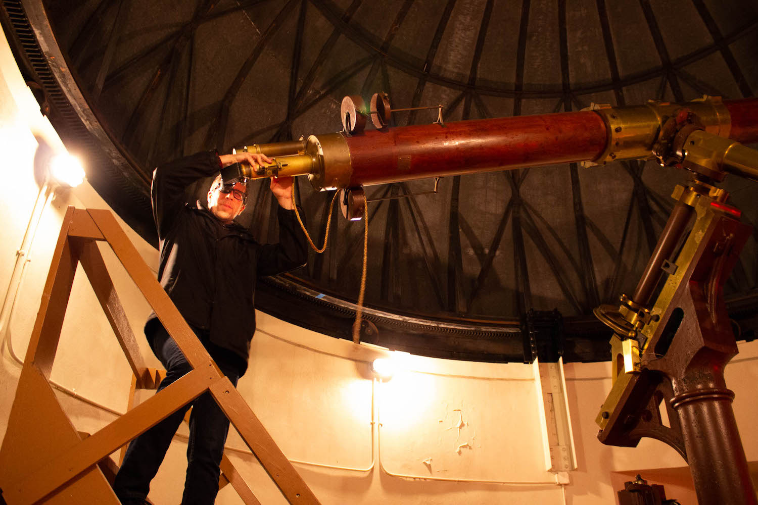 a man looking through a large wooden telescope in an observatory