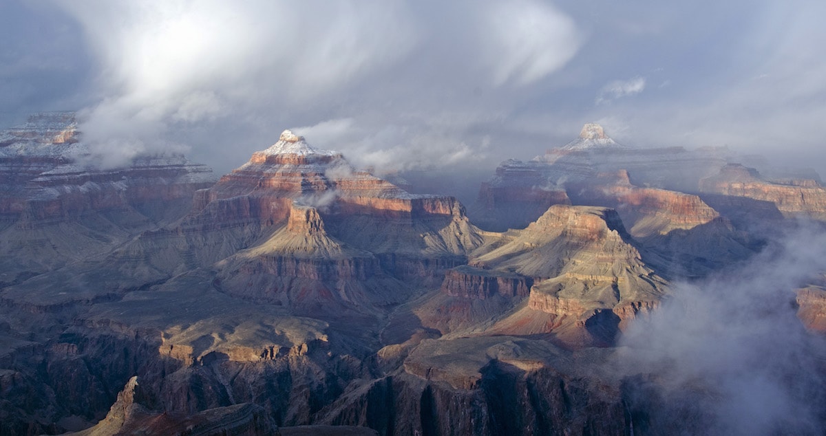 a real photo of the grand canyon with some of the peaks covered in snow on a grey cloudy day