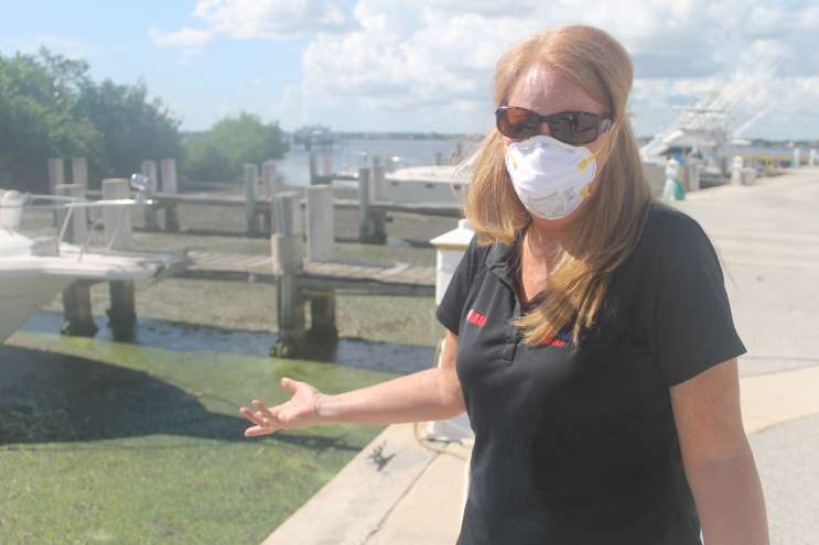 woman on pier with sunglasses and surgical mass gesturing to a lake with algae