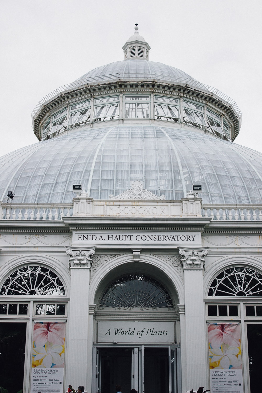 The exterior of a greenhouse with a domed glass roof. above the front entrance it says "enid a. haupt conservatory" and "a world of plants"