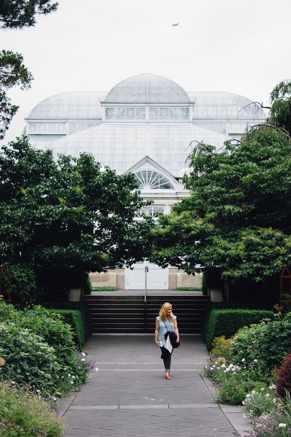 woman walking among gardens with greenhouse behind her