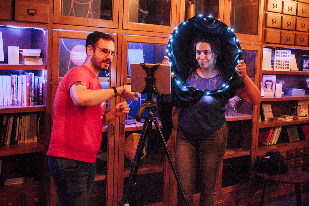 two people standing in front of an ipad taking a photo with a black hole constructed from hula hoop and fabric 