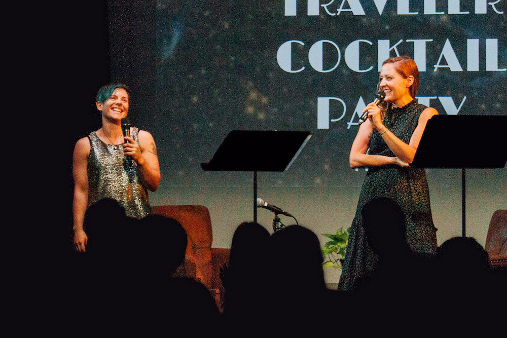 two people on stage laughing and talking into mics