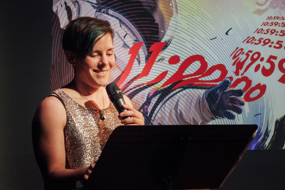 woman with mic on stage with abstract art projected behind her