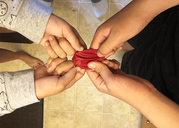 two pairs of hands holding an unstretched red balloon