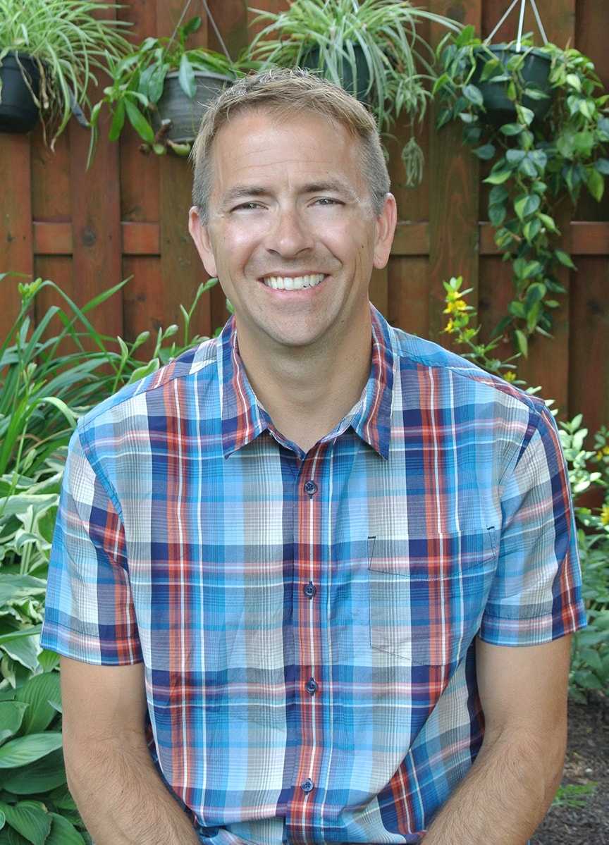 Jeff Grant sitting in front of a fence and hanging plants