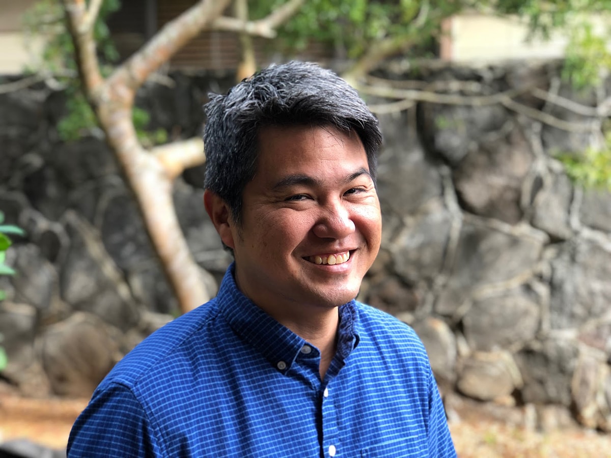 Randy Otaka standing in front of a tree and brick wall