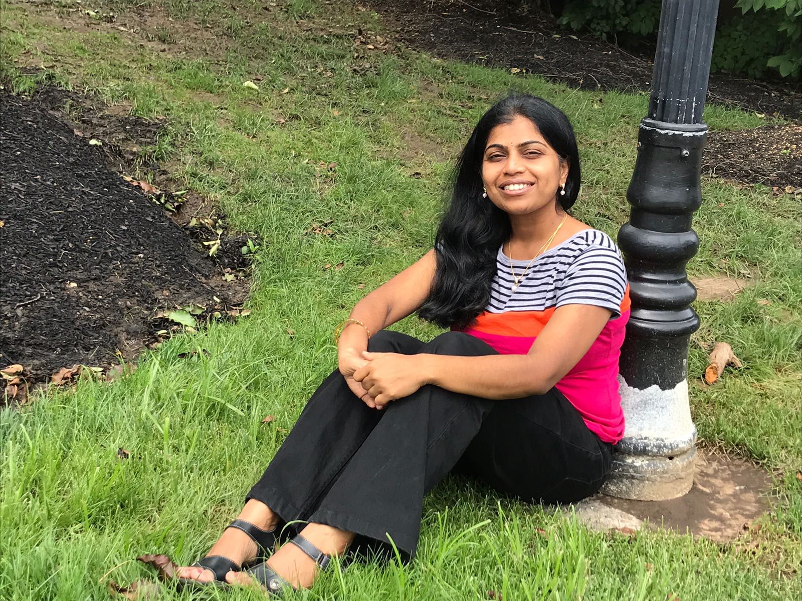 Srividhya Sundaram sitting on the grass at the based of a light pole 