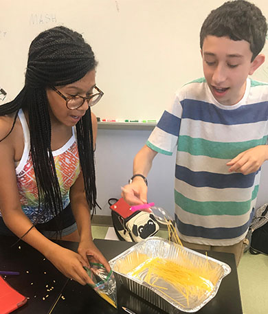 a female african american teacher assisting a student with the food collection setup of the experiment