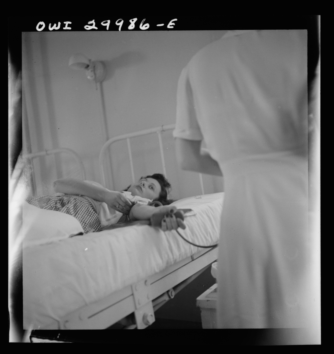 a woman lies in bed donating blood to a nurse in the 1940s