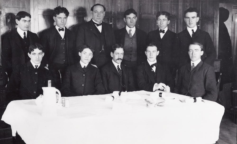 black and white photo of eleven men in suits sitting around a white table clothed table