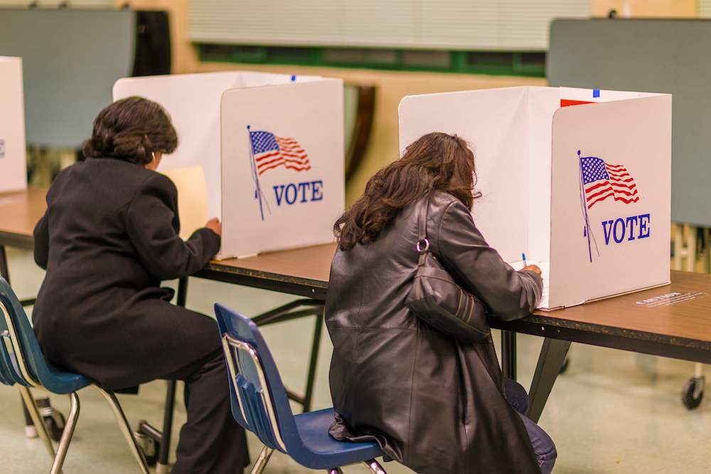 two women sitting at a table each working in her own voting booth