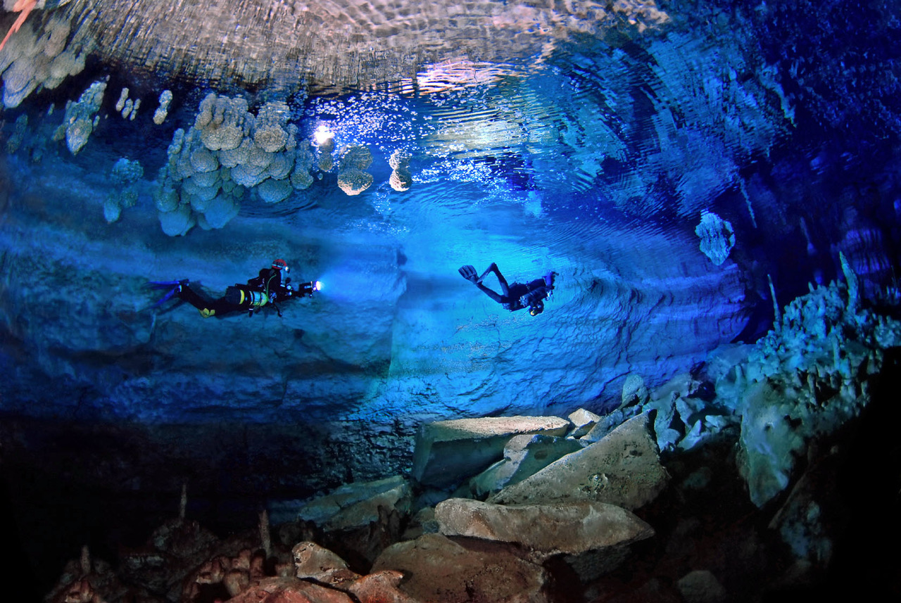 underwater shot of two divers with flashlights surrounded by different rock formations