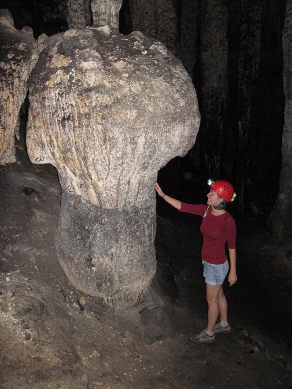 woman in hard hat touching a mushroom-shaped rock about twice her size