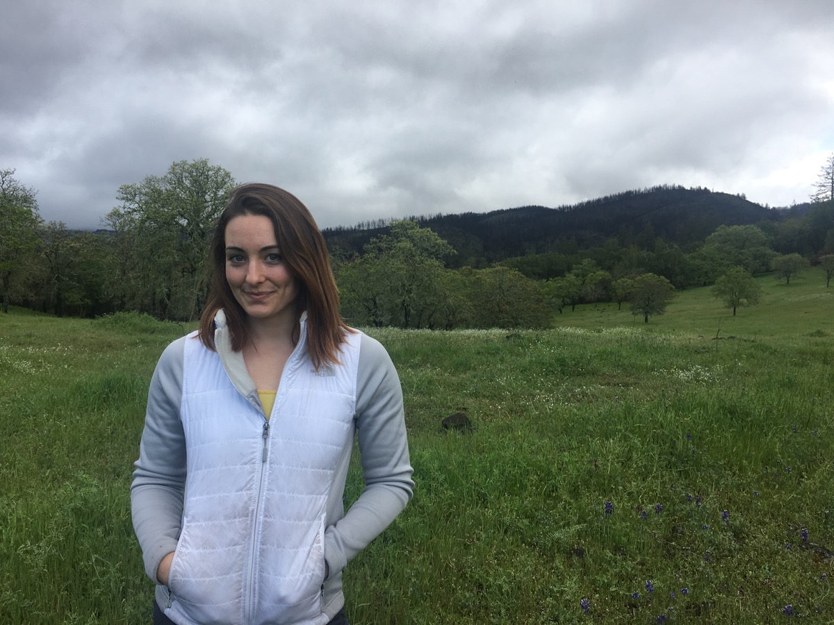 a woman standing in a grassy field under an overcast sky