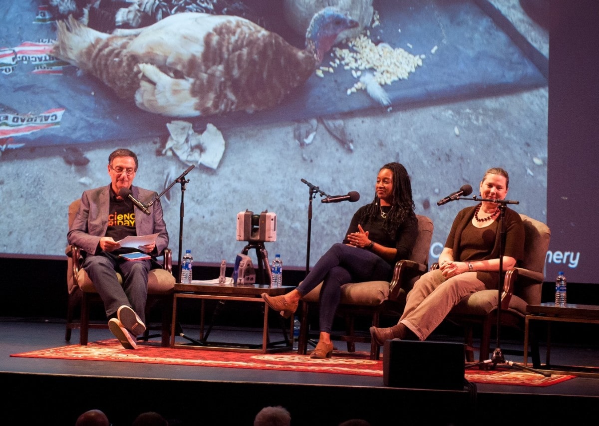 a man interviews two archaeologists, a black woman and a Caucasian woman, on stage. there is a slide of a turkey in the background