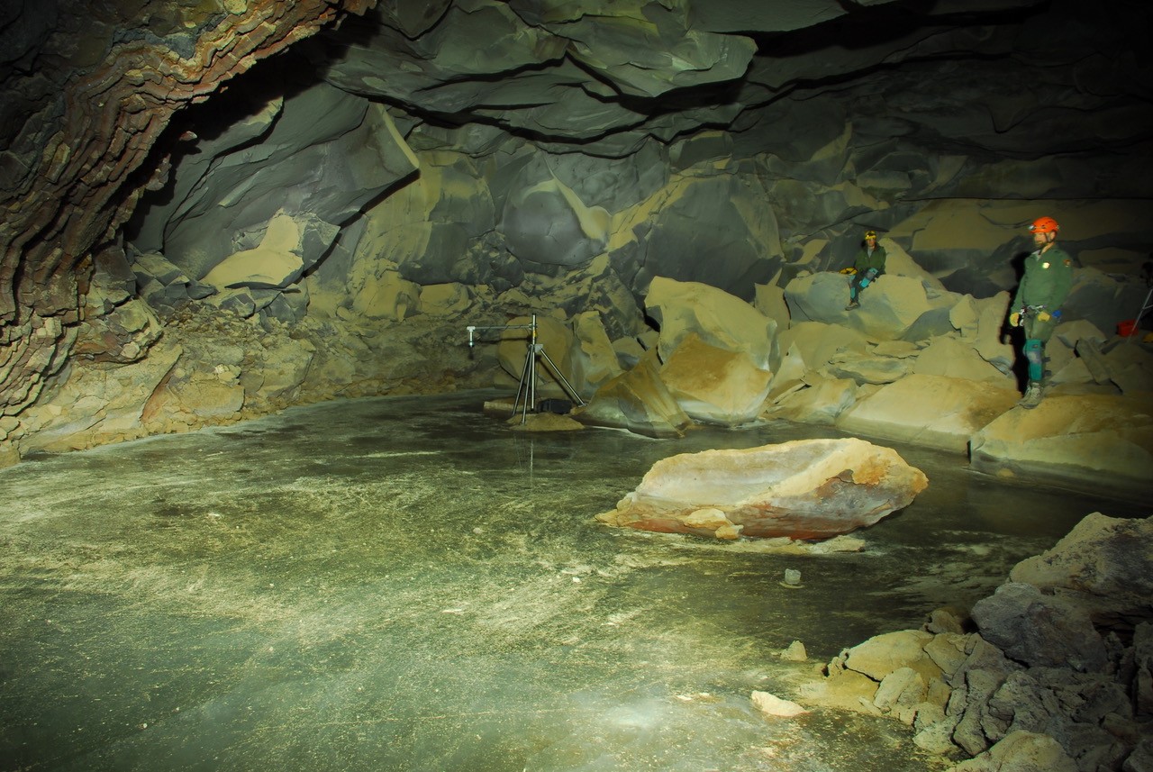 two people with safety gear in a cave standing at the edge of ice lake