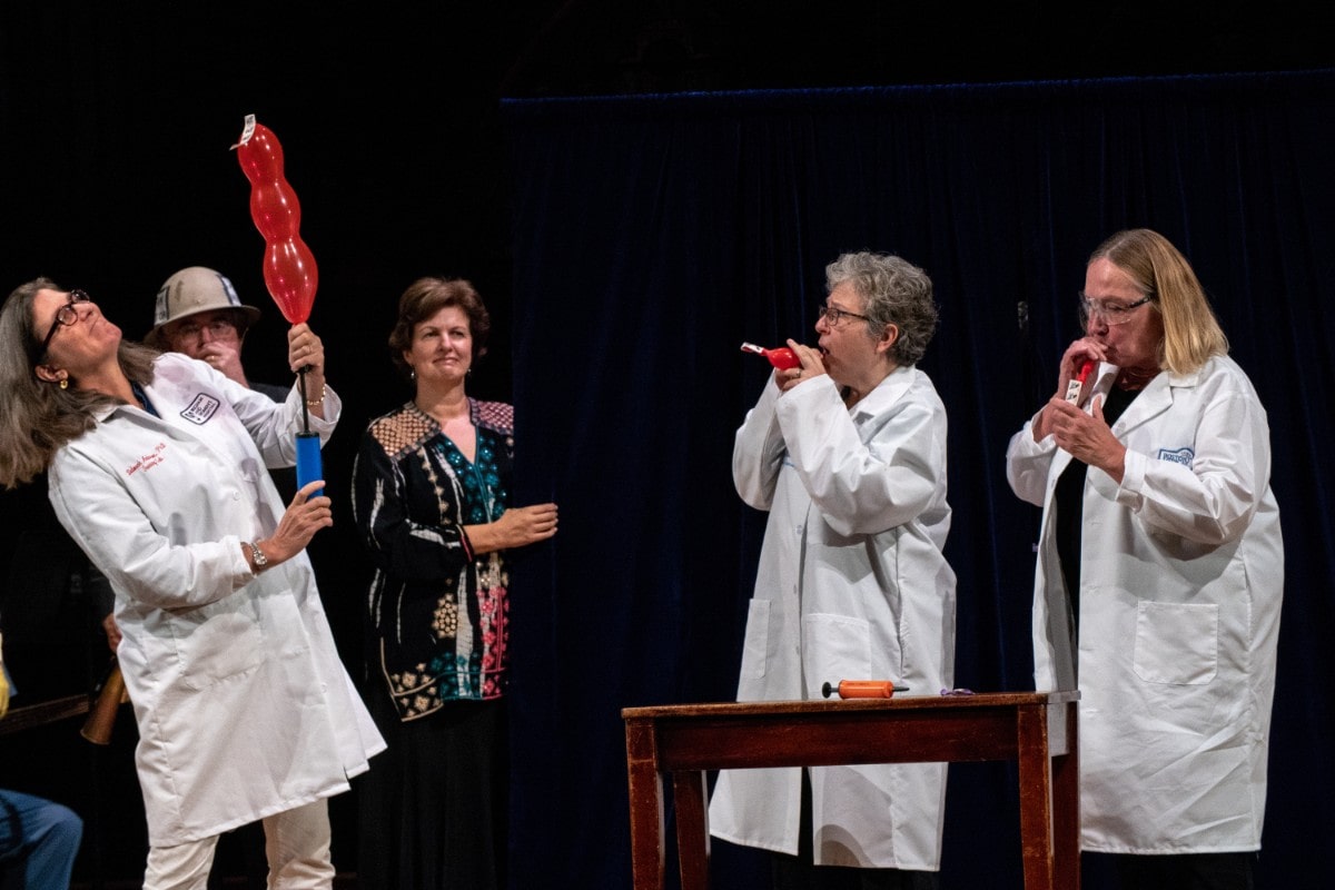 three women in lab coats doing a demonstration on stage