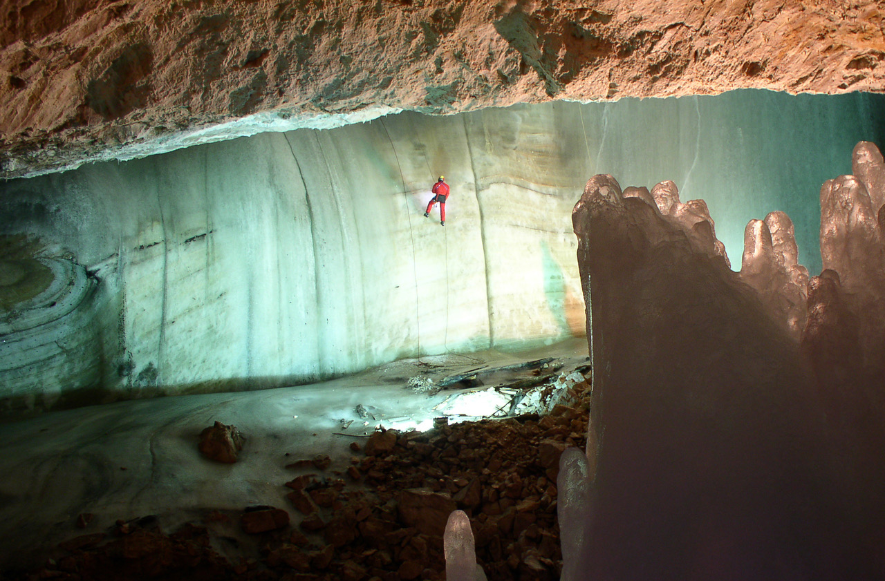 interior of cave with man in orange safety gear scaling down an ice wall