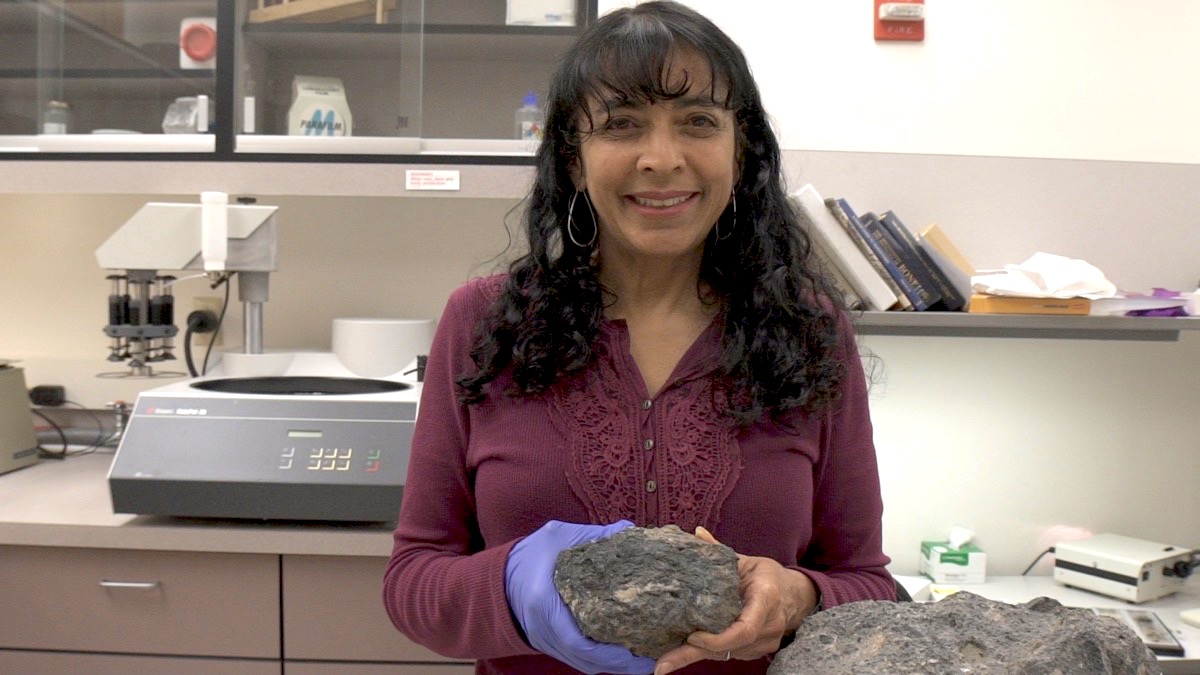 a woman holds a large rock (the coprolite) with both hands in a lab