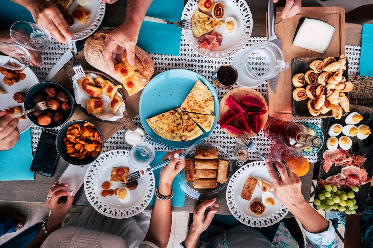 aerial view of spread of food with multiple hands reaching for it