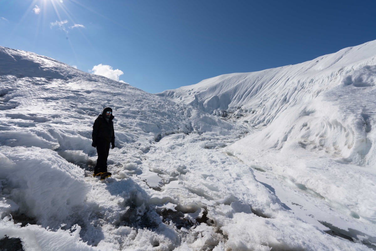 A figure in bundled in dark cold weather clothes, standing on a giant glacier