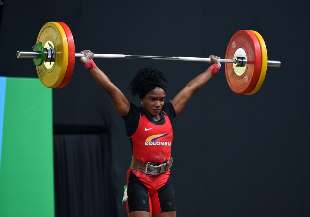 a colombian woman holds flyweights over her head at a competition