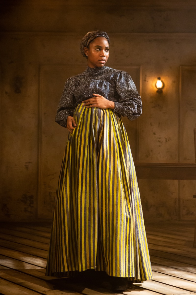 a woman of color dressed in 19th-century servant garb. she's pregnant and has her hand over her belly