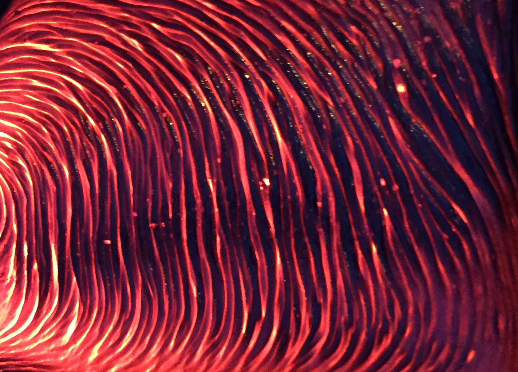 a close up of bright red glow peaks between ripples and folds of hot lava.