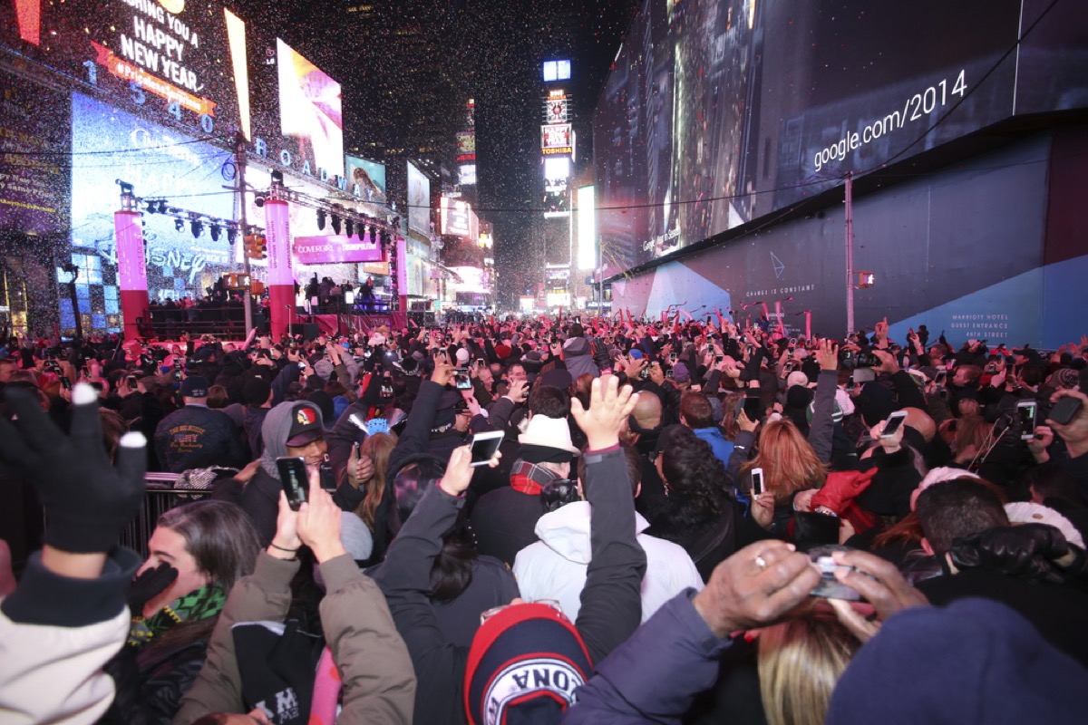 a massive crowd of people celebrating and raising their arms up at midnight with confetti in the air. in new york city