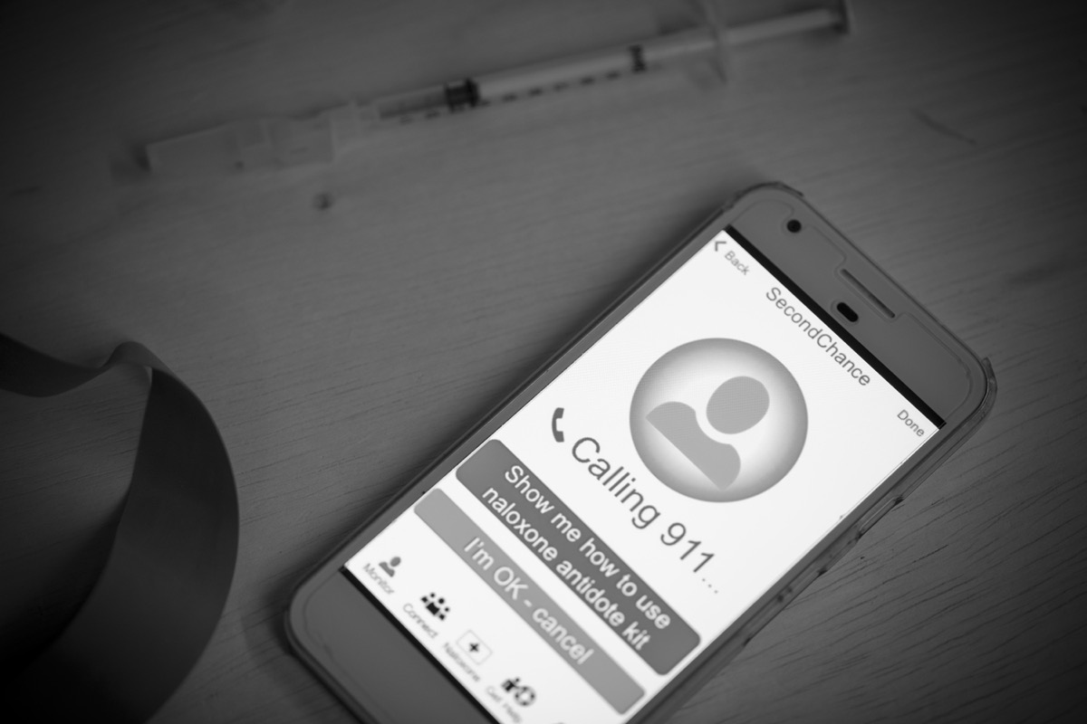 black and white image of a smartphone displaying a screen with options to learn how to administer naloxone or cancel the call
