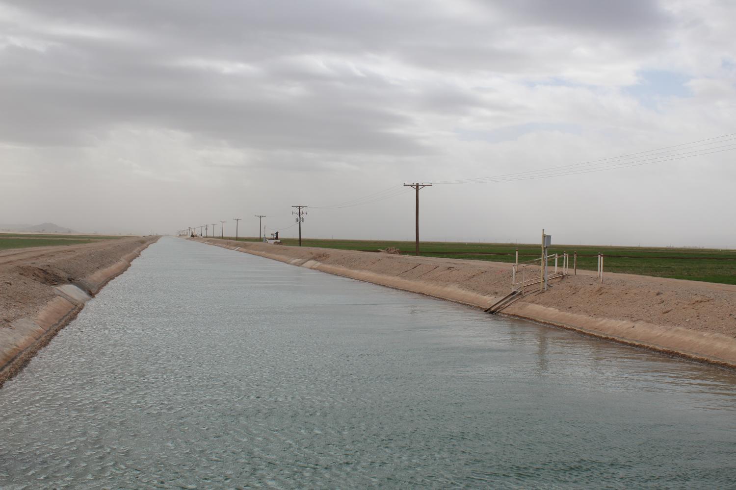 A wide flat canal stretches into the distance with power lines running alongside it