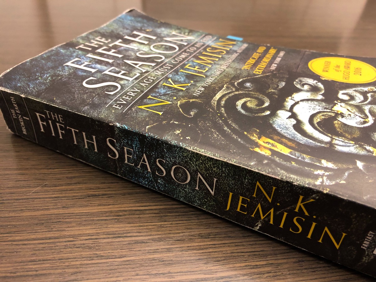 copy of 'the fifth season' with swirling patters on the cover sitting on a wood table