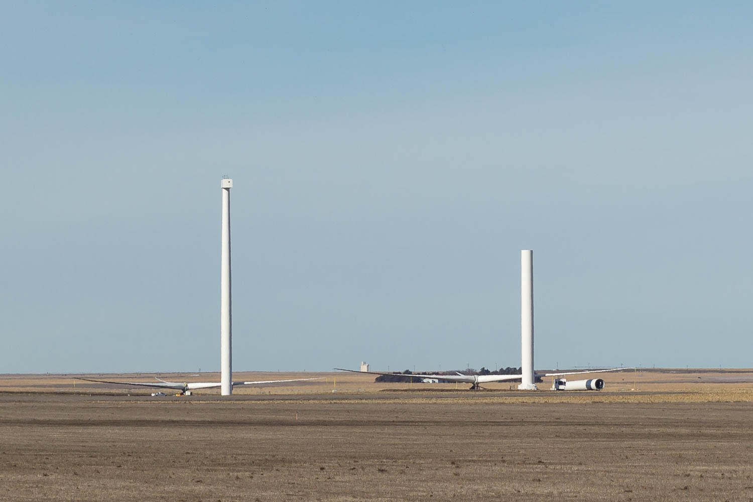 just the poles of two wind turbines in a field, with the remaining pieces on the ground