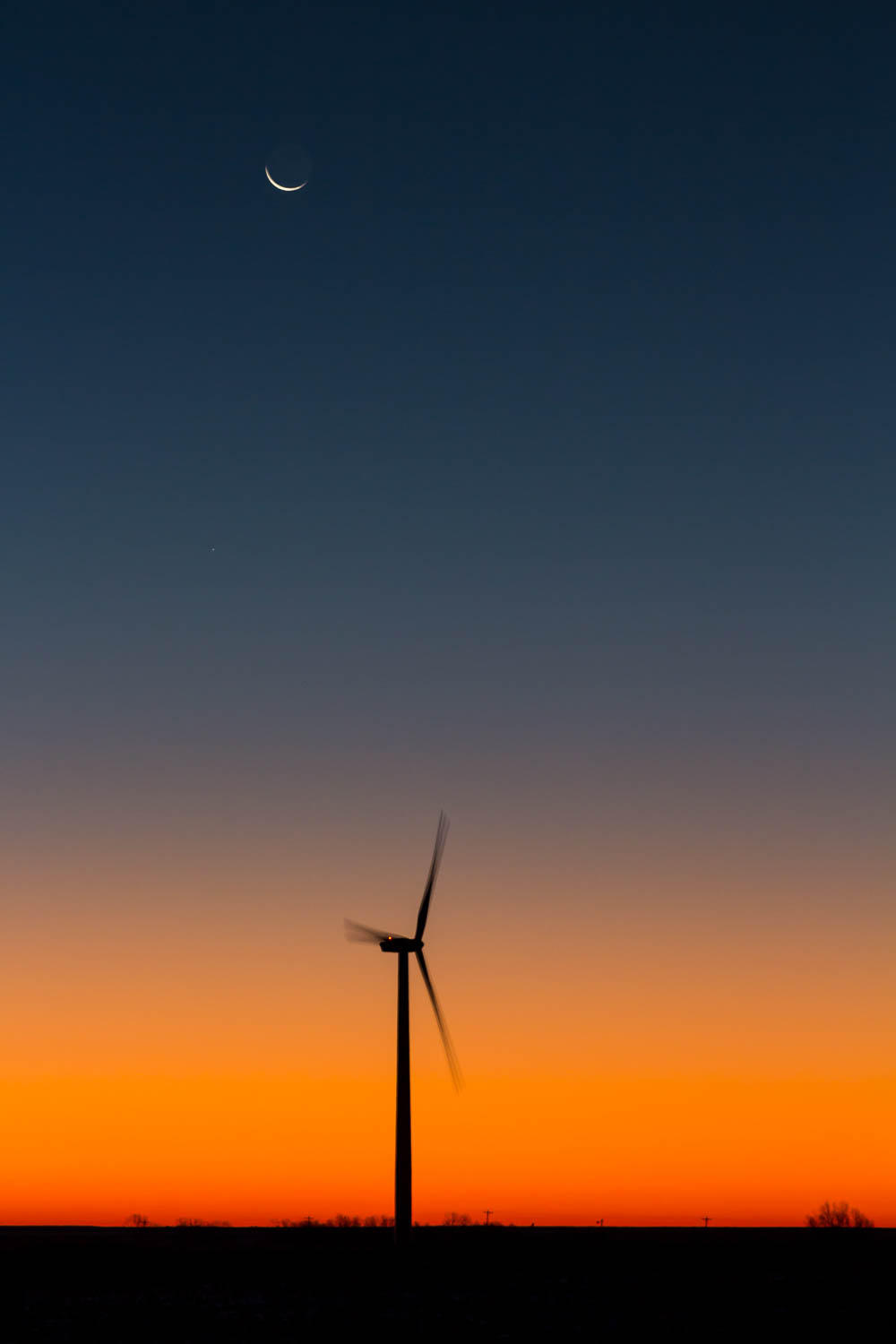 a wind turbine set against the morning sky with a crescent moon at the top of the frame