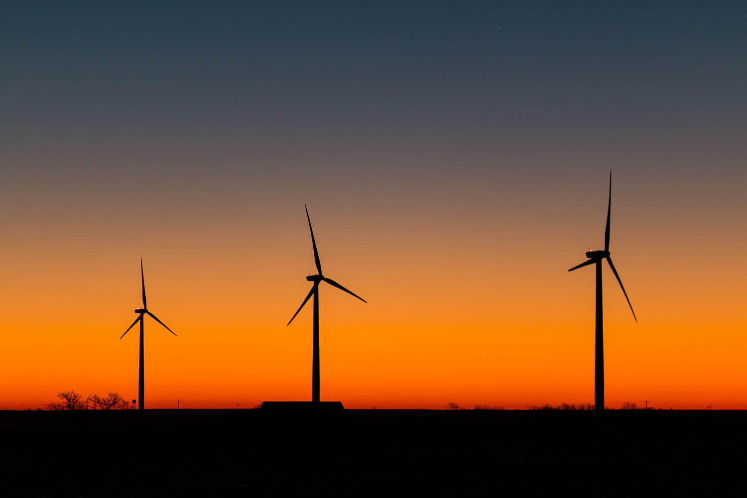 three wind turbines silhouetted against a setting sun