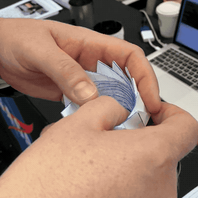 an animated gif of two hands unfolding and easily refolding an origami circular paper