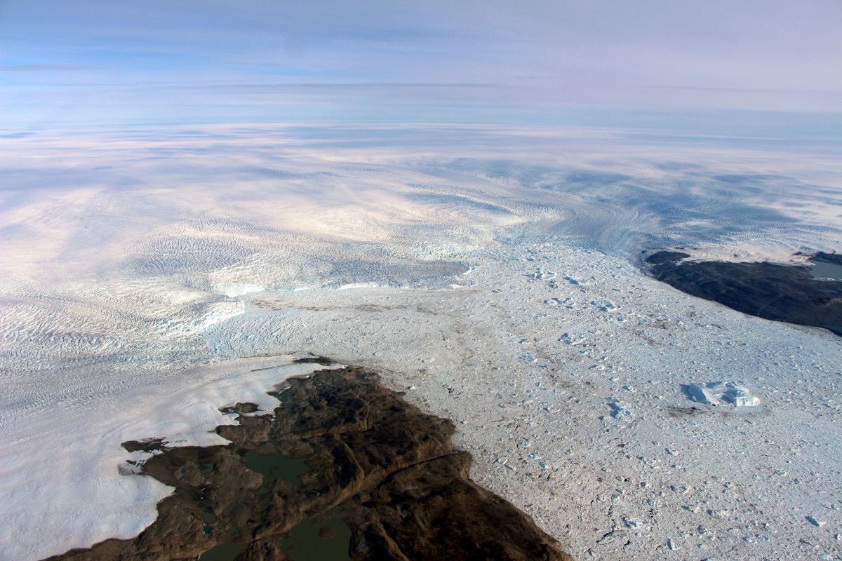 the edge of a glacier as seen from the air, which is releasing icebergs into the ocean.