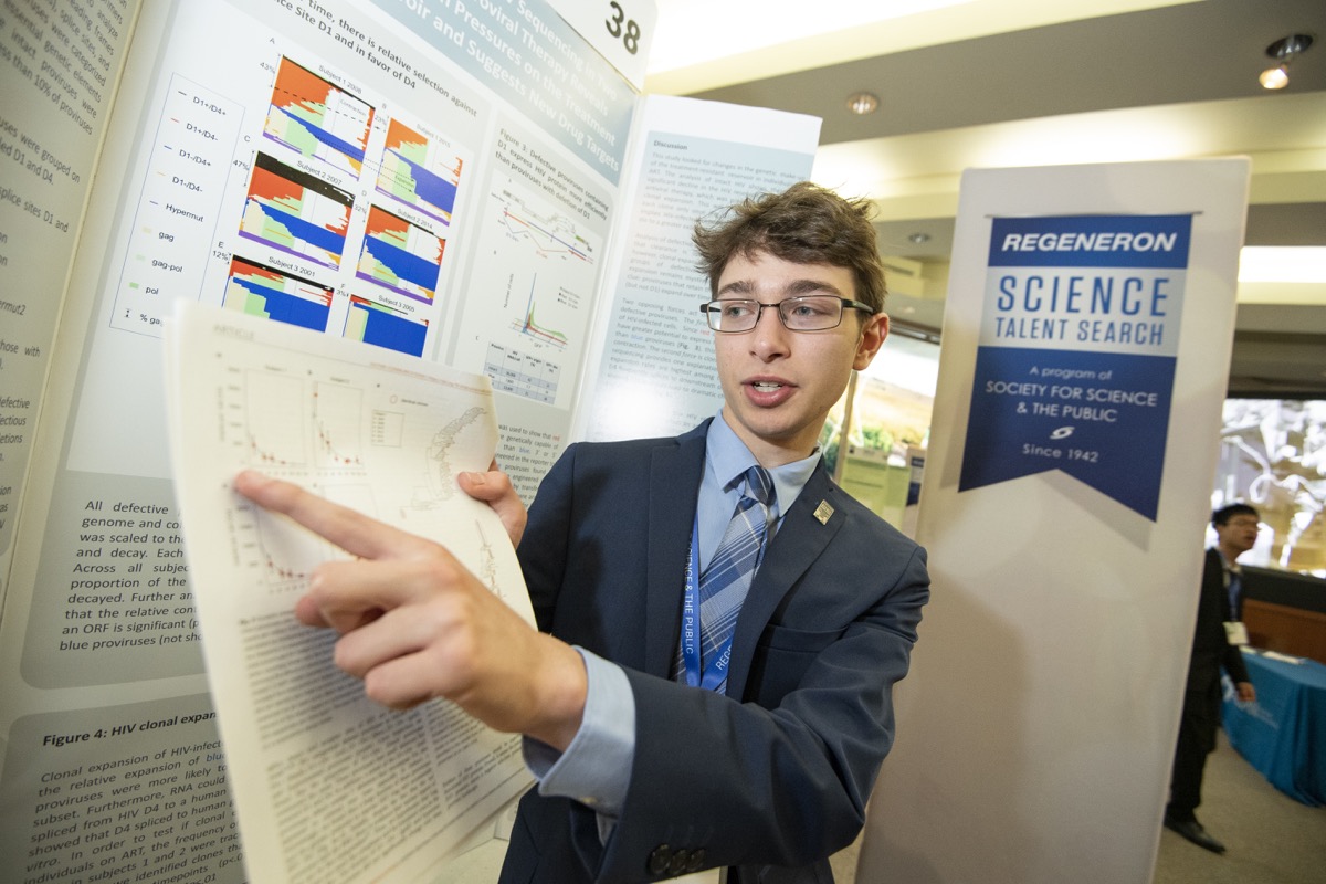 a boy stands in front of a poster board display and points to a piece of paper 