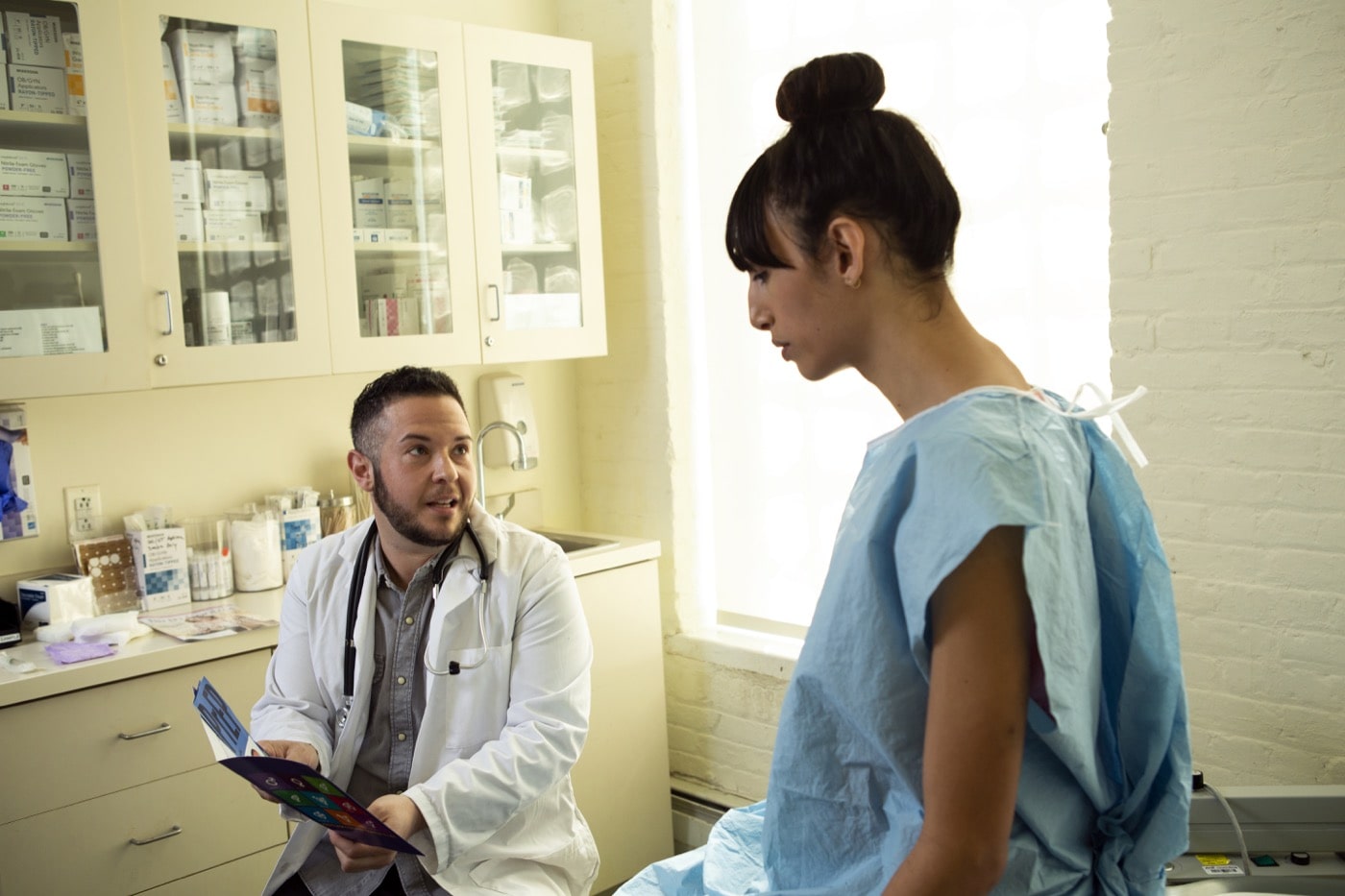 A patient in a hospital gown speaking to her doctor in an exam room.