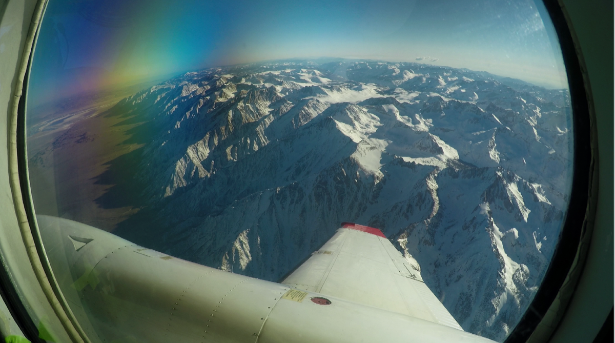 view out the window of a plane wing observing snow on mountains