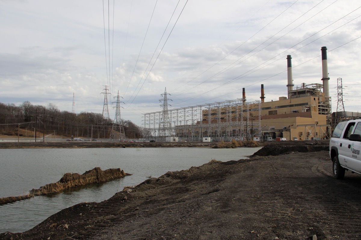 a coal power plant under an overcast sky. next to it in the foreground is a large pool of water that looks more like a lake than a pond