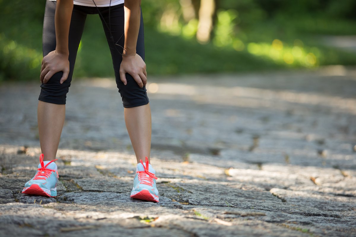 woman bent over on a road wearing running tights and shoes and resting after a workout